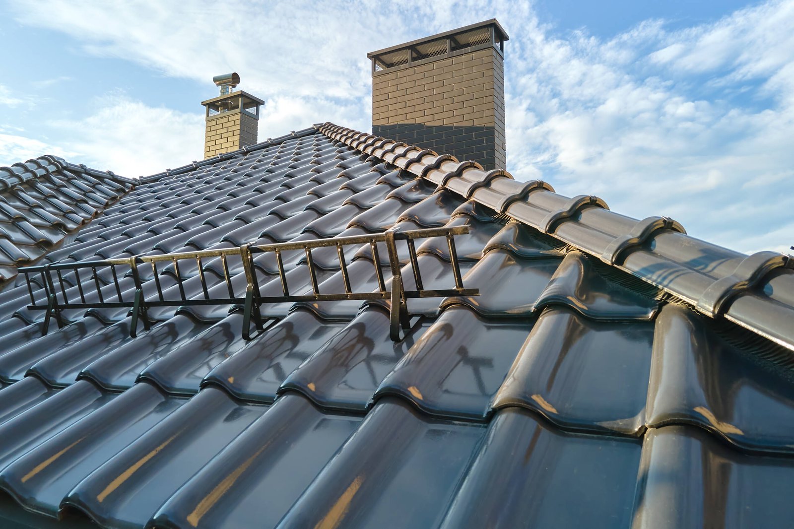 Closeup snow guard for safety in winter on house roof top covered with ceramic shingles. Tiled covering of building.